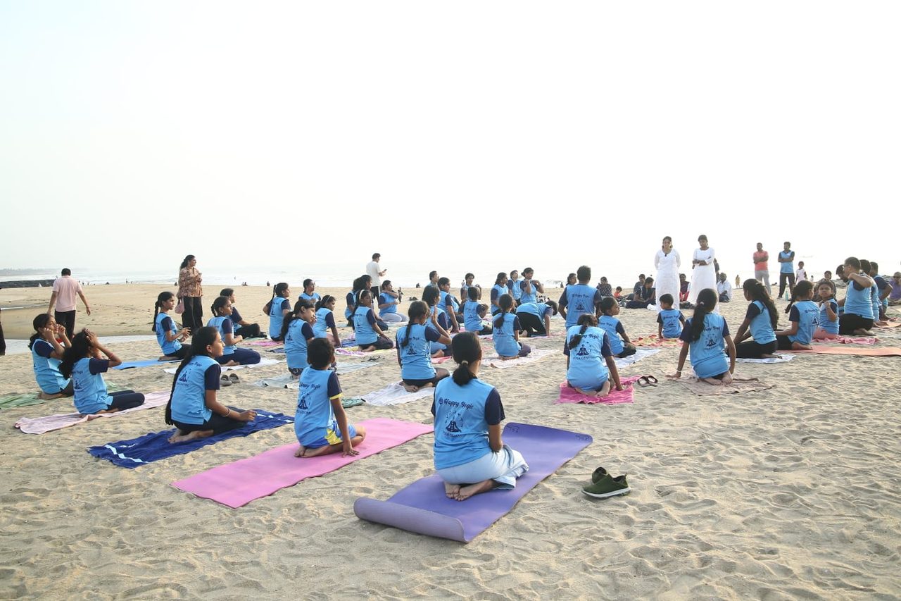 Students seated on mats at a Happy Yogis beach session, the sea behind them