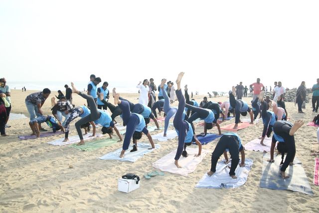 Students in a wide-legged forward bend together on the sand