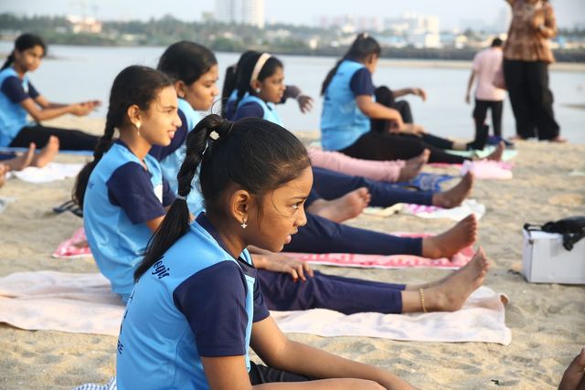A row of students in a seated forward bend, the city skyline behind