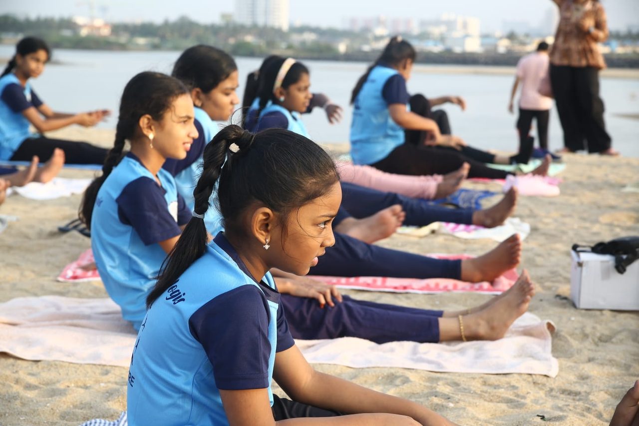 A row of students in a seated forward bend, the city skyline behind