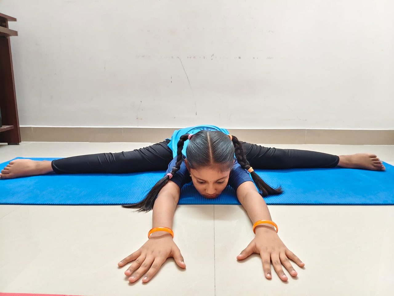 A student holding a wide-legged seated forward fold on a mat at the centre