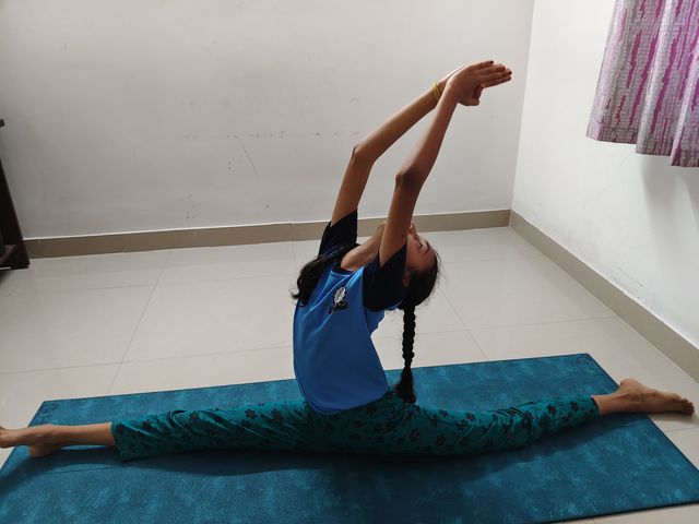 A student in a seated side split, arms stretched overhead