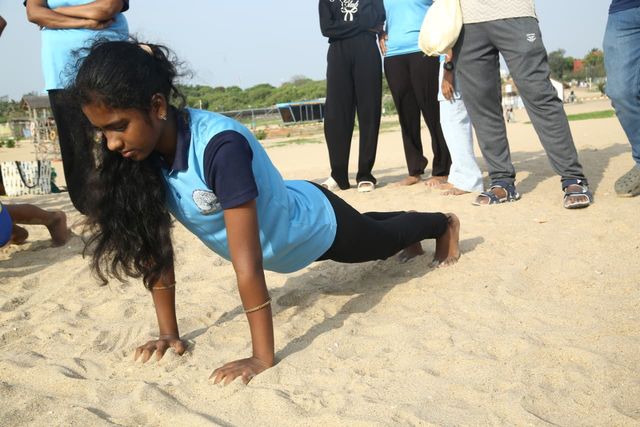 A student lowering into the plank of a sun salutation on the sand