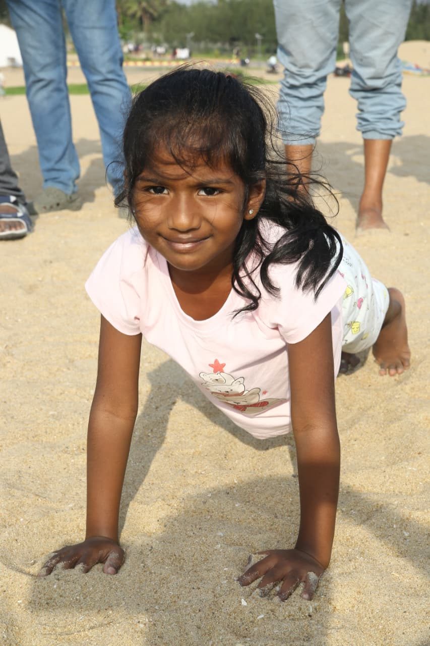A young girl on her hands in the sand, smiling at the camera